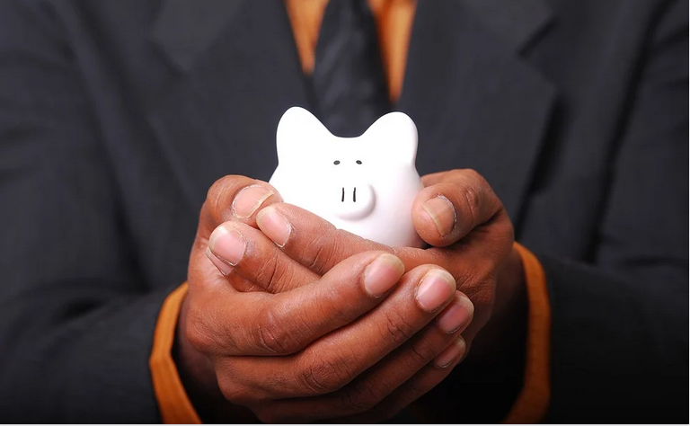 A man holding a piggy bank in his folded palms to depict the culture of saving in order to achieve financial independence